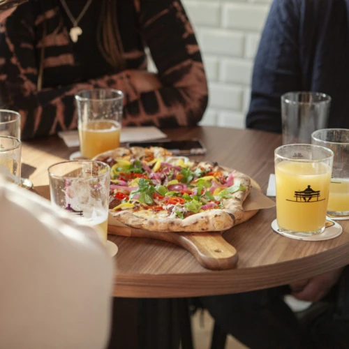 Närbild på ett bord där några personer sitter runt. I mitten står en nygräddad pizza och personerna har öl i deras glas.