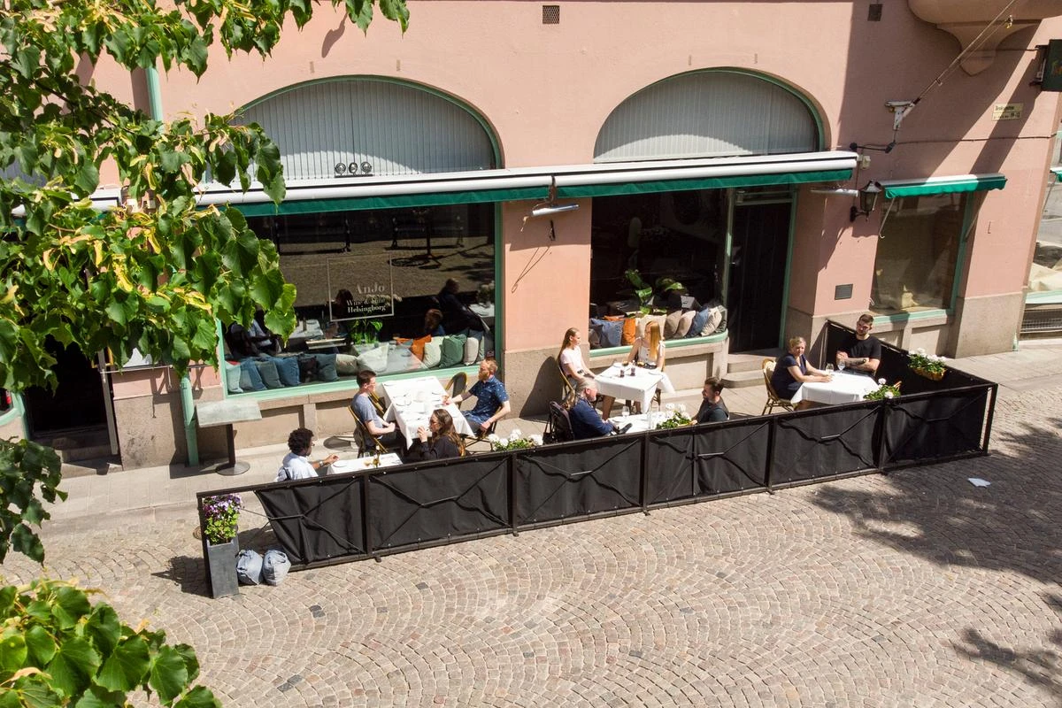 Uteserveringen på AnJo Wine och Dine en sommardag. Flera bord med vita dukar och personer som äter lunch.