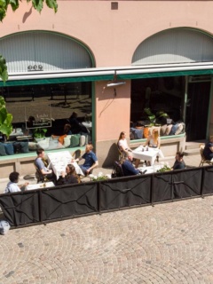 Uteserveringen på AnJo Wine och Dine en sommardag. Flera bord med vita dukar och personer som äter lunch.