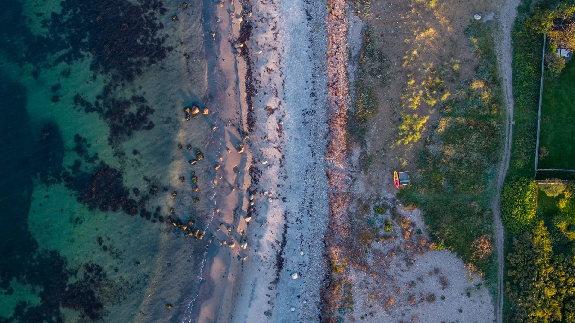 Drönarbild över Kullaleden, en smal stig slingrar sig mellan stranden och gröna områden.