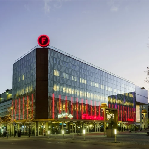 Kvällsbild över gallerian Söder. Hus med glaspartier formade som trianglar. Filmstadens F högst upp på taket.