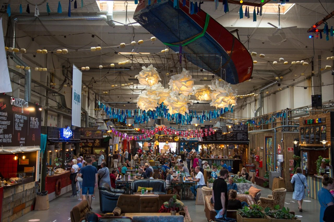 Värvets matmarknad i Helsingör. Kreativ miljö med danska flaggor i taket och olika vimplar. Ett myller av folk som äter och umgås.