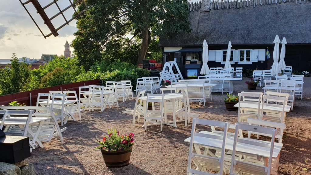 Sommarbild från Möllebackens restaurang och cafe. Utsikt lver sundet och rådhuset. På gårdsplanen står vita gammaldags trämöblemang och i bakgrunden syns ena längan med tidstypiskt halmtak.