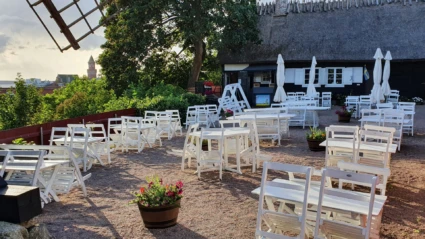 Sommarbild från Möllebackens restaurang och cafe. Utsikt lver sundet och rådhuset. På gårdsplanen står vita gammaldags trämöblemang och i bakgrunden syns ena längan med tidstypiskt halmtak.