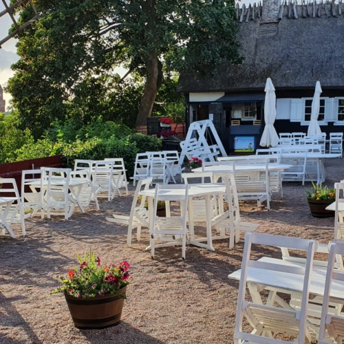 Sommarbild från Möllebackens restaurang och cafe. Utsikt lver sundet och rådhuset. På gårdsplanen står vita gammaldags trämöblemang och i bakgrunden syns ena längan med tidstypiskt halmtak.