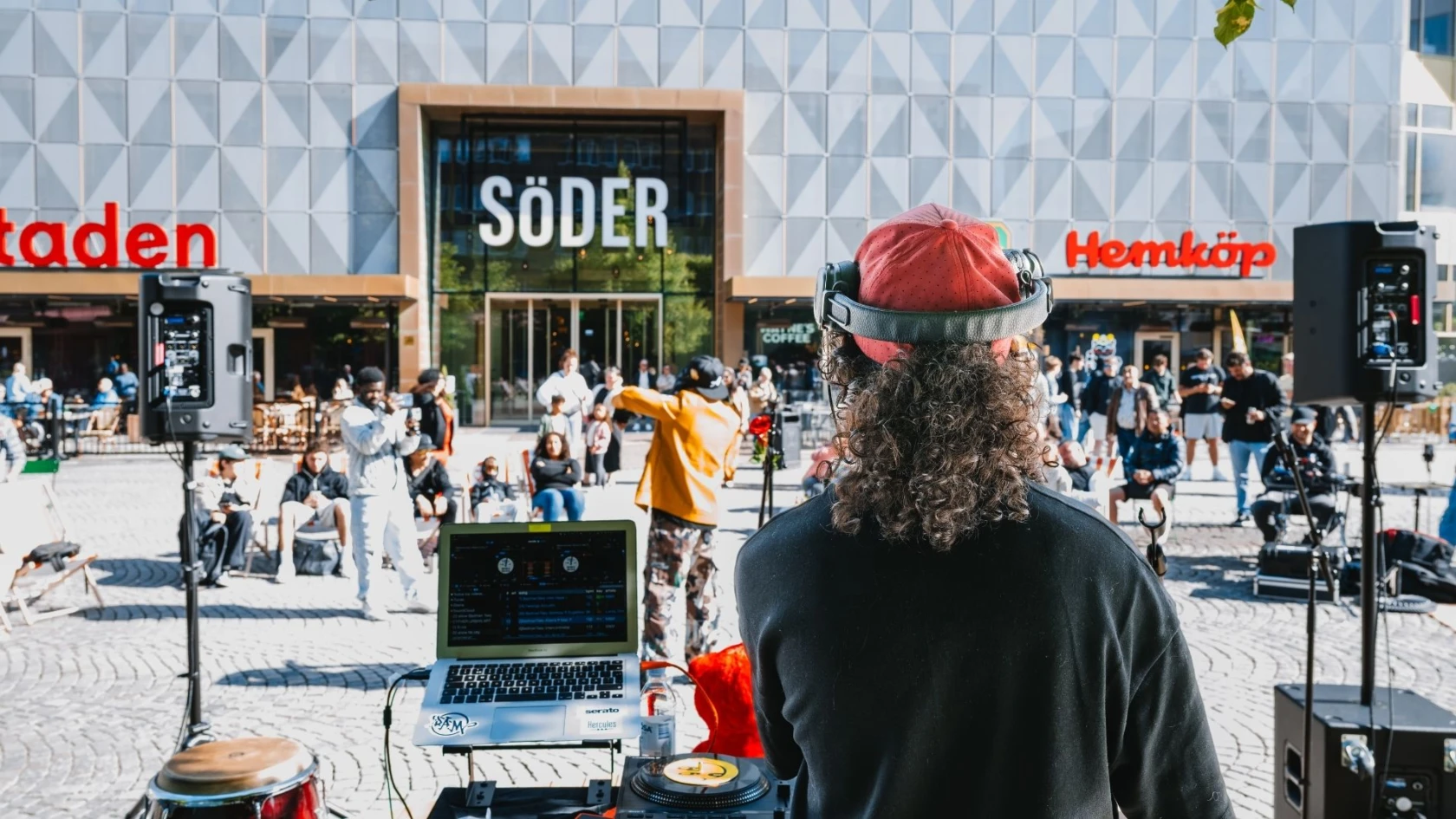 Mäster palms plats med en DJ och folk som hänger i solen.