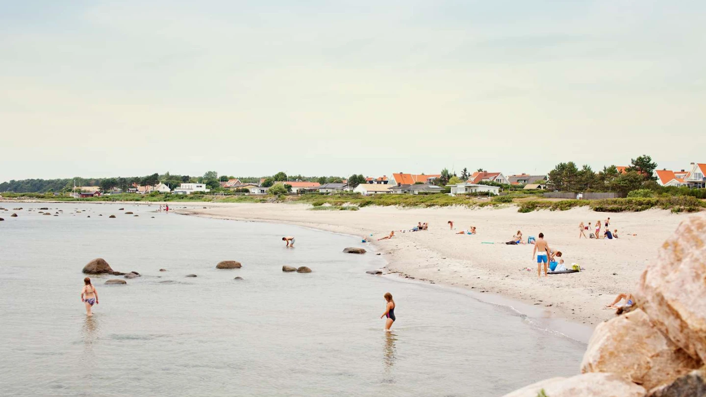 Bad på stranden i Domsten, villor skymtar i bakgrunden.