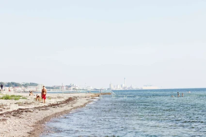 Badande på Vikingstrand i Helsingborg, staden skymtar i bakgrunden.