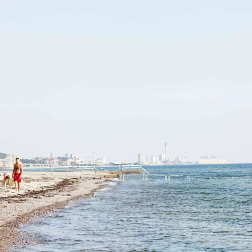 Badande på Vikingstrand i Helsingborg, staden skymtar i bakgrunden.