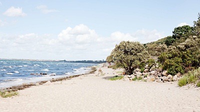 Rydebäcks strand med grönska vid strandkanten och vita böljande vågor på sundet.