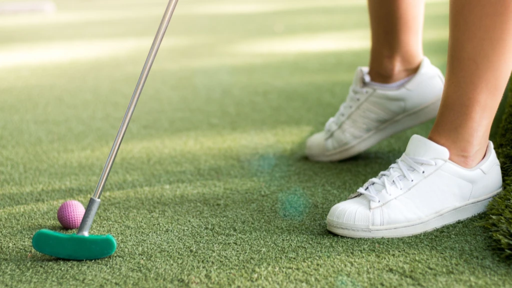 Närbild på minigolfbana med en persons om håller i en klubba med rosa boll.