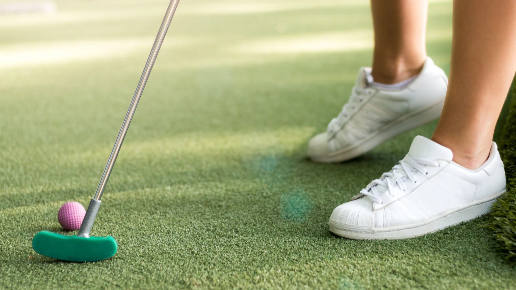 Närbild på minigolfbana med en persons om håller i en klubba med rosa boll.