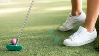 Närbild på minigolfbana med en persons om håller i en klubba med rosa boll.