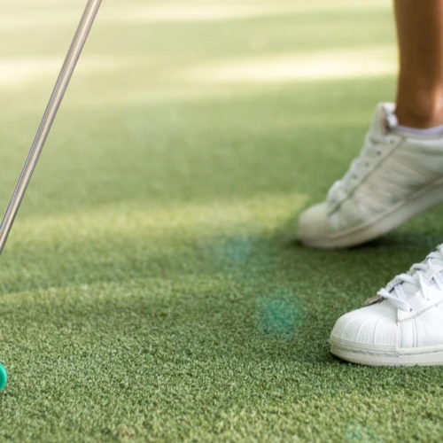 Närbild på minigolfbana med en persons om håller i en klubba med rosa boll.