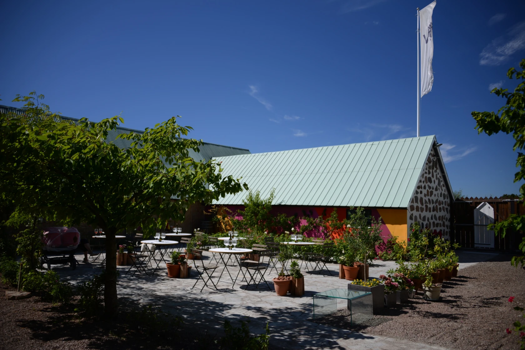 Innergården på Vejby vingård med en länga i röda toner och en stensatt altan med små bord för att sitta ner och smaka på vinerna.