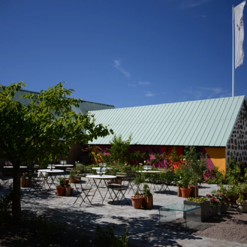 Innergården på Vejby vingård med en länga i röda toner och en stensatt altan med små bord för att sitta ner och smaka på vinerna.