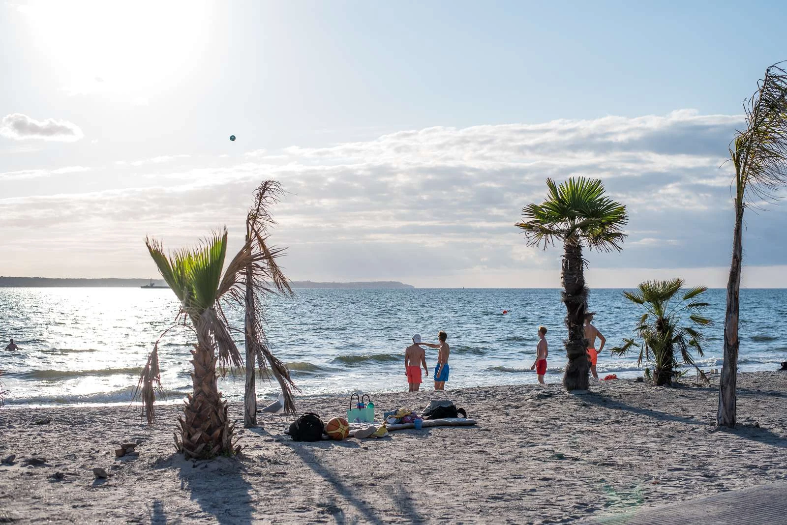 Tropical beach med vajande palmer. Några ungdomar hänger vid strandkanten