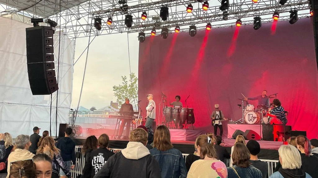 Ett konserttält med ett band som spelar på scen. Lampor lyser i rött och publiken står framför scenen.