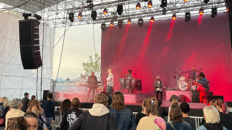 Ett konserttält med ett band som spelar på scen. Lampor lyser i rött och publiken står framför scenen.