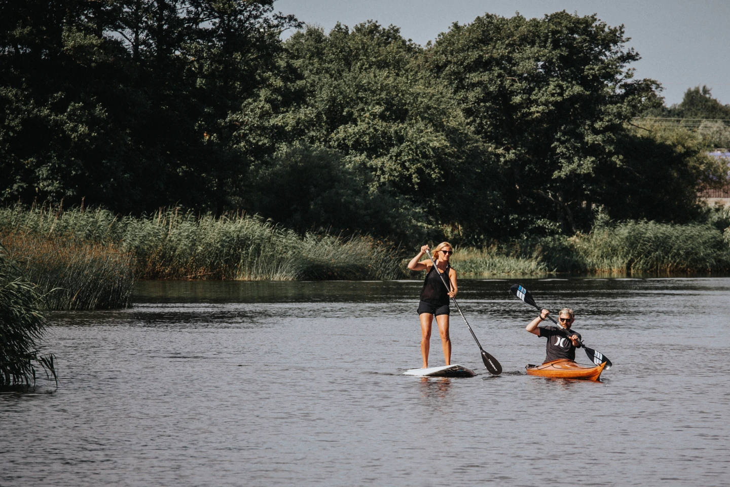 Två personer paddlar kajak och sup på Rönneå.