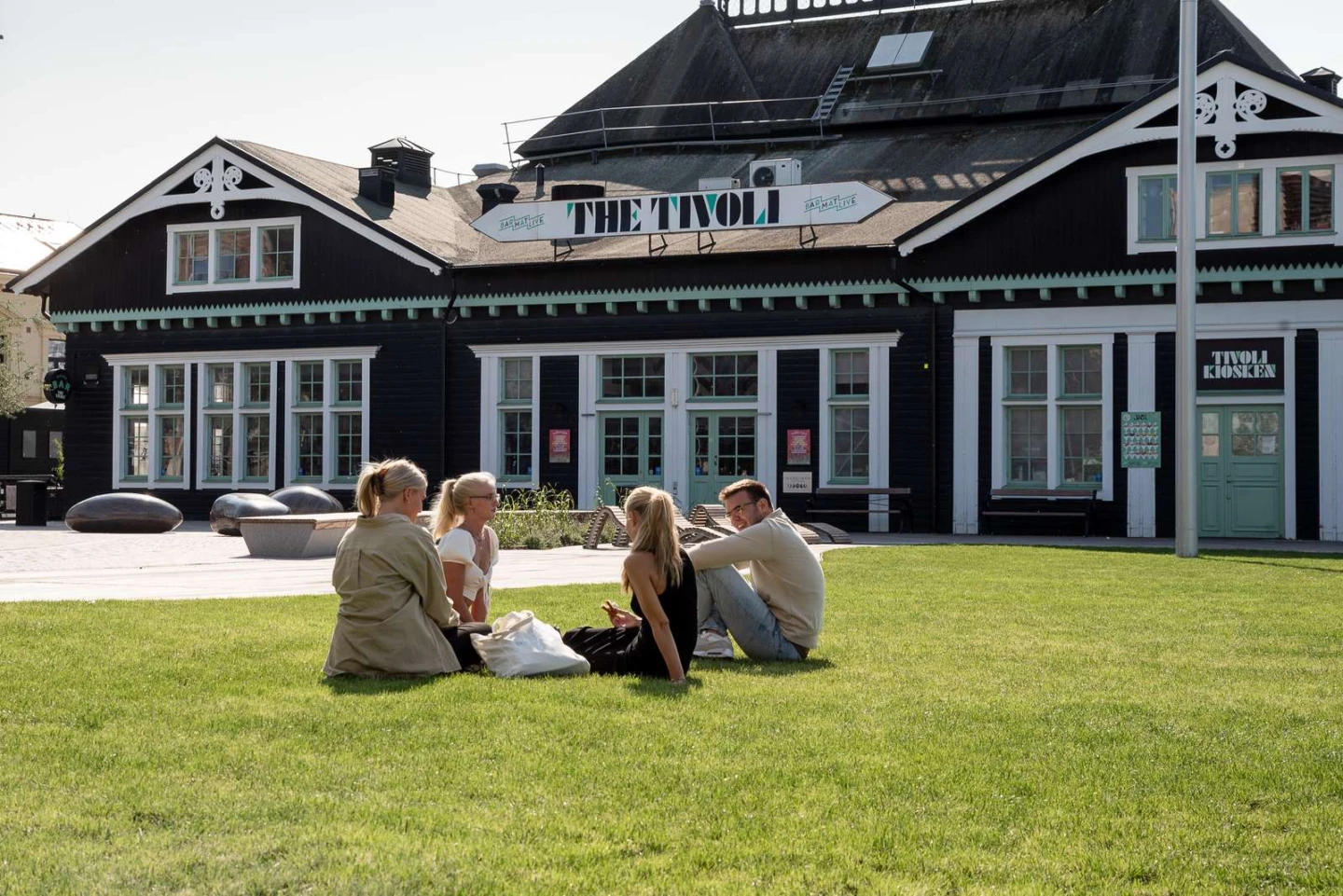 Fyra personer sitter på en gräsmatta framför The Tivoli.
