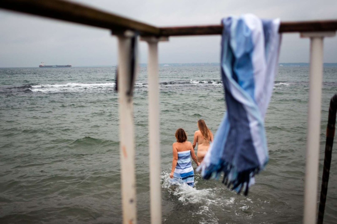 Två kvinnor kallbadar i havet. I förgrunden hänger en blå handduk.