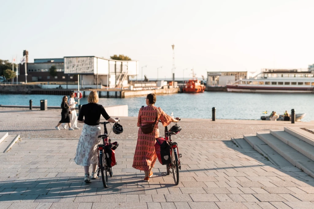 två personer går med varsin cykel ner mot kajkanten