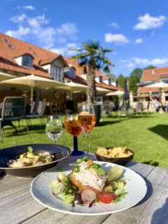 Mat och dryck på bord utomhus. Byggnad med palmer i bakgrunden, blå himmel
