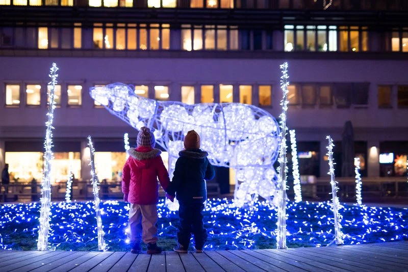 Två barn håller hand framför en stor ljusinstallation som föreställer en isbjörn