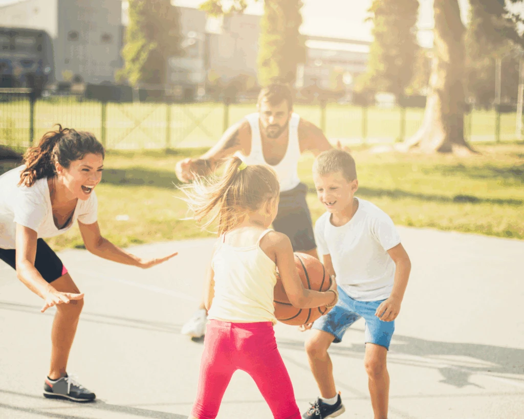 mamma, pappa och två barn spelar basket utomhus