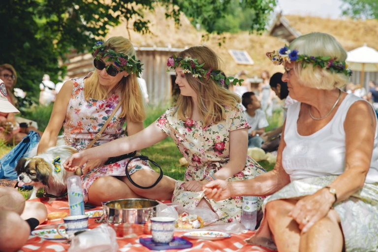 midsommarfika på en filt. Sommarklänningar och kransar på 3 kvinnor.