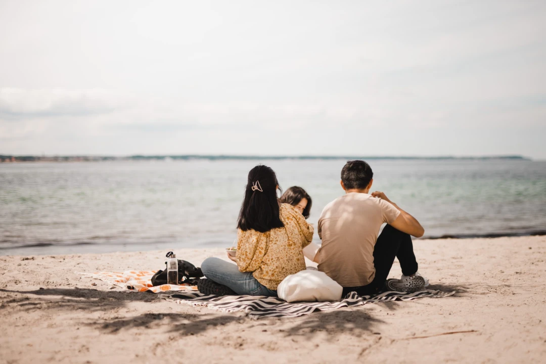 Bild på två studenter, man och en kvinna, som sitter med ryggen mot kameran på stranden och blockar ut över havet