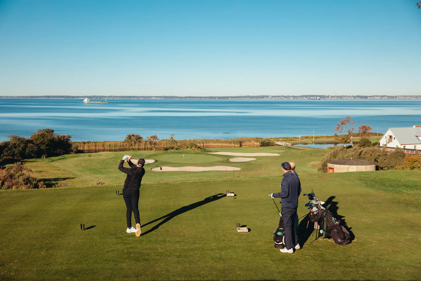2 golfare svingar ut med sundet och danmark som bakgrund