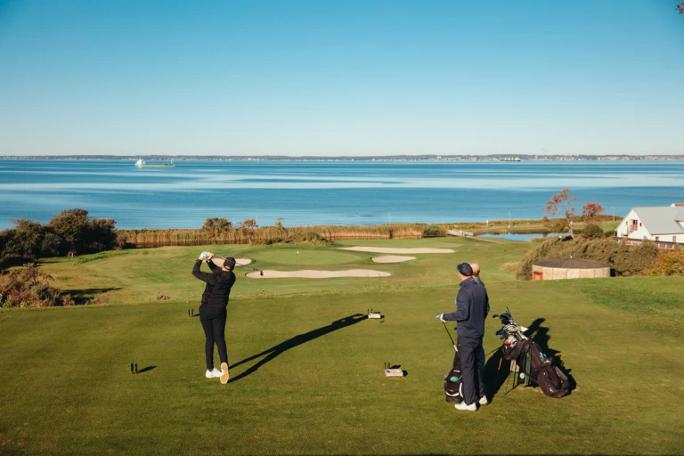 2 golfare svingar ut med sundet och danmark som bakgrund