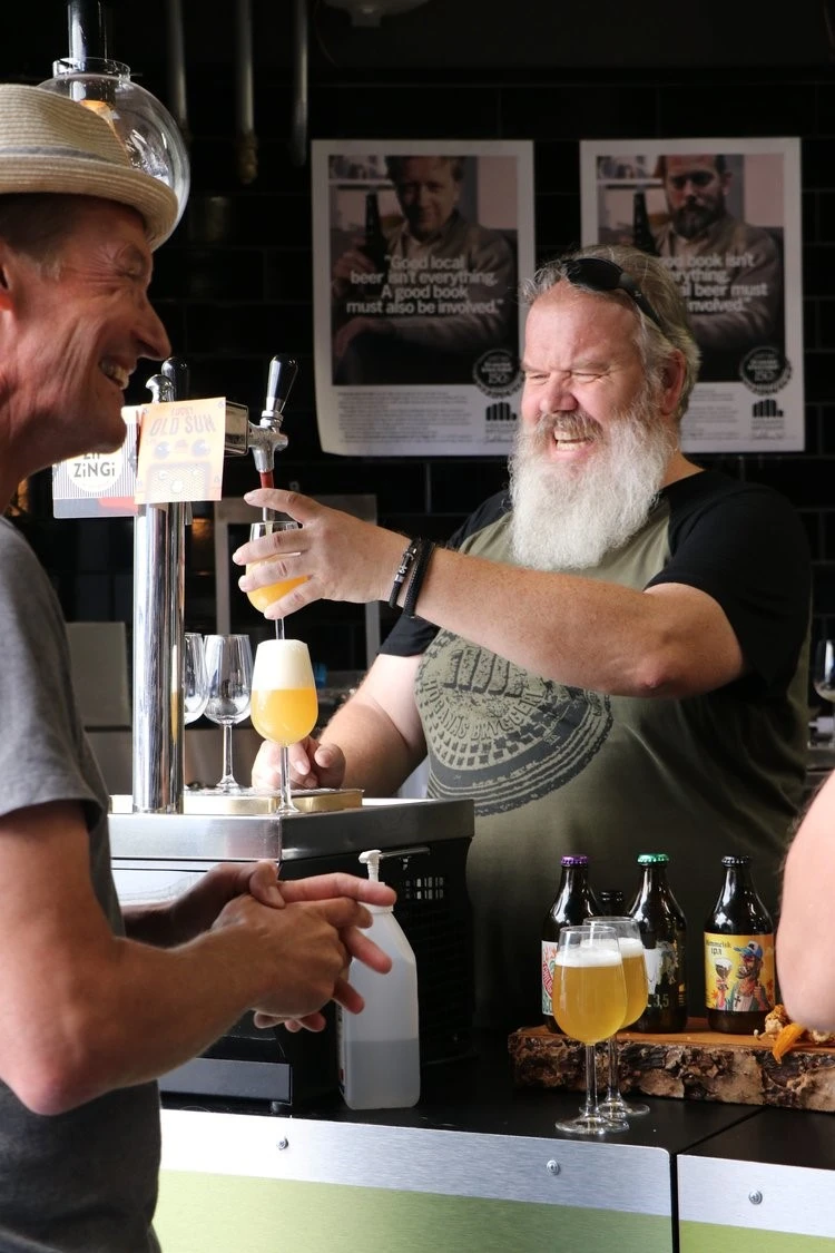 en person med skägg häller upp öl i en bar från en tapp.