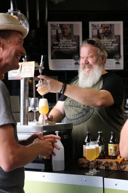 en person med skägg häller upp öl i en bar från en tapp.