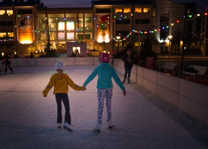 2 barn håller hand och åker skridsko på en utomhus isbana