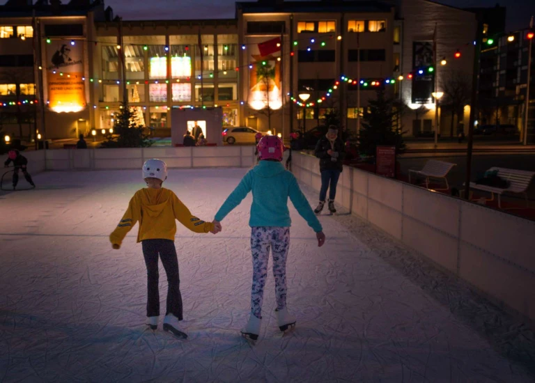 2 barn håller hand och åker skridsko på en utomhus isbana