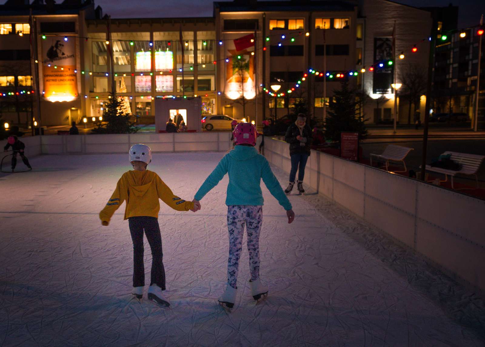 2 barn håller hand och åker skridsko på en utomhus isbana