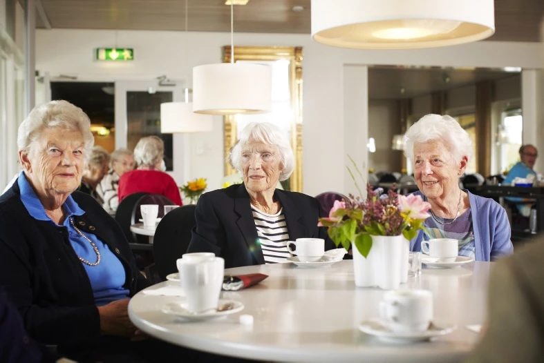 Tre kvinnor sitter runt ett bord och dricker kaffe