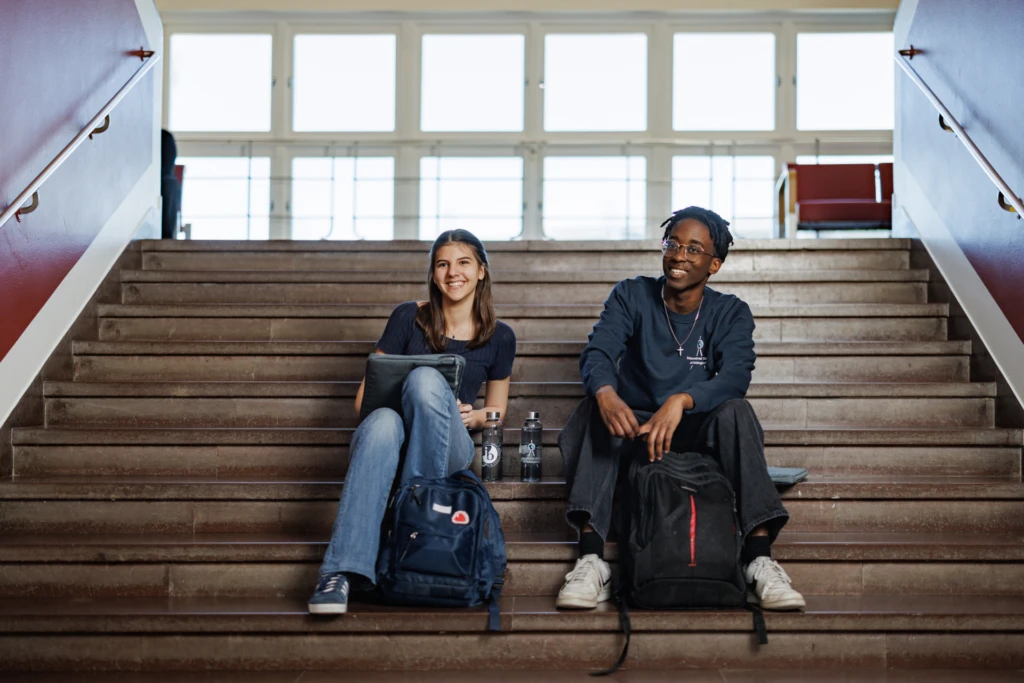 Two students hanging out on a staircase at school.