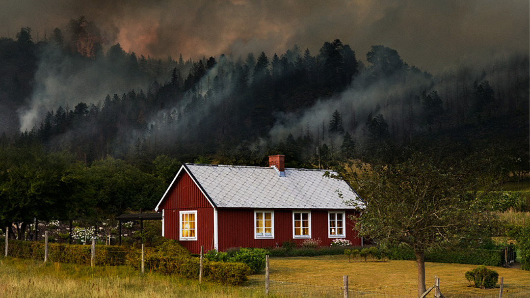 Hus med skogsbrand i bakgrunden