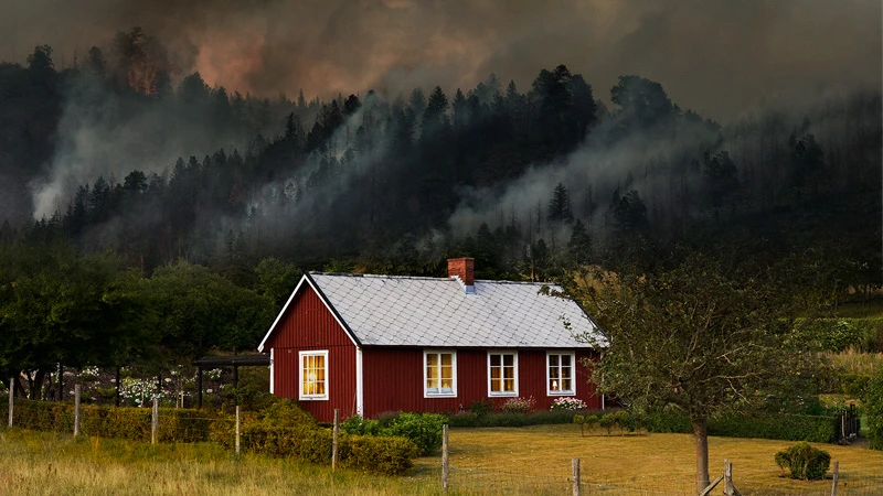 Hus med skogsbrand i bakgrunden