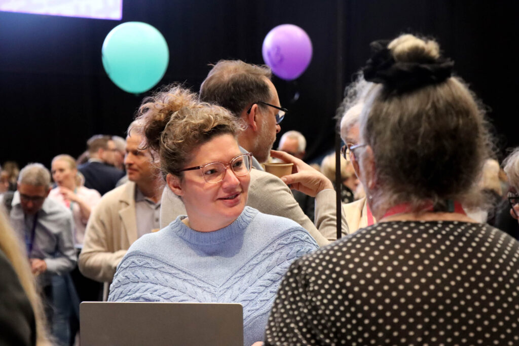 Personer i samtal vid ett evenemang med ballonger i bakgrunden.