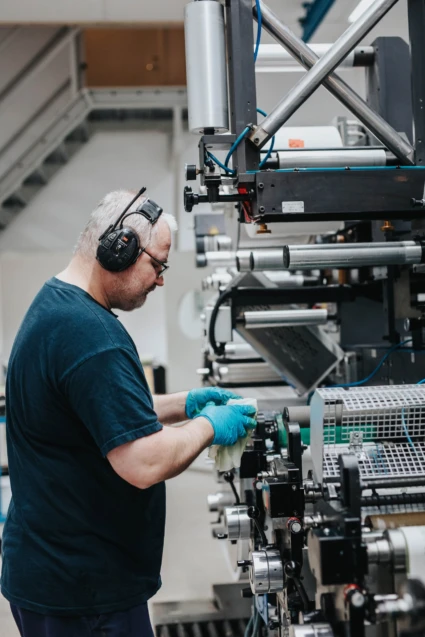 Man med hörselkåpor arbetar vid en industriell maskin.
