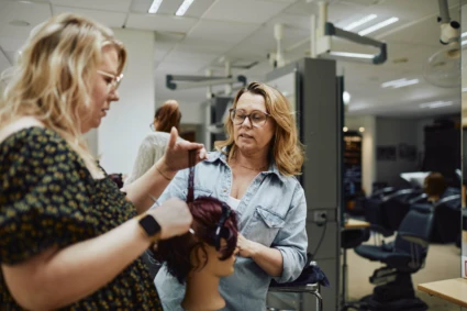 En frisörlärare visar en elev hur man stylar hår.