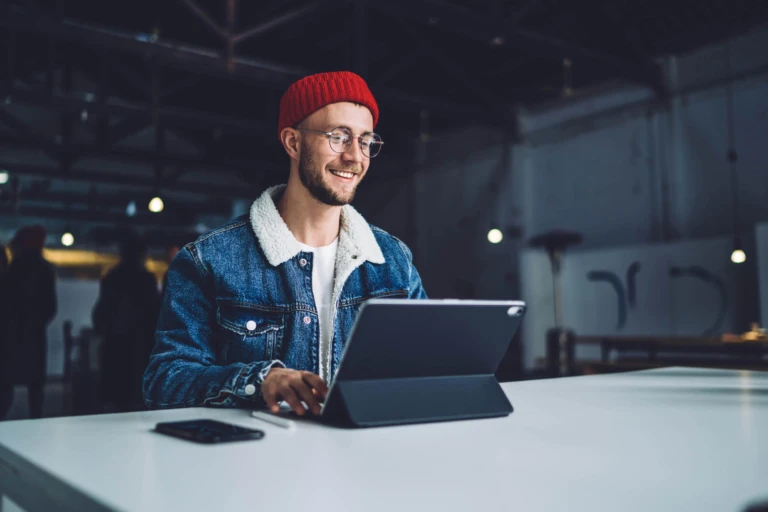 Kille med glasögon, jeansjacka och röd mössa som leendes tittar på sin platta.