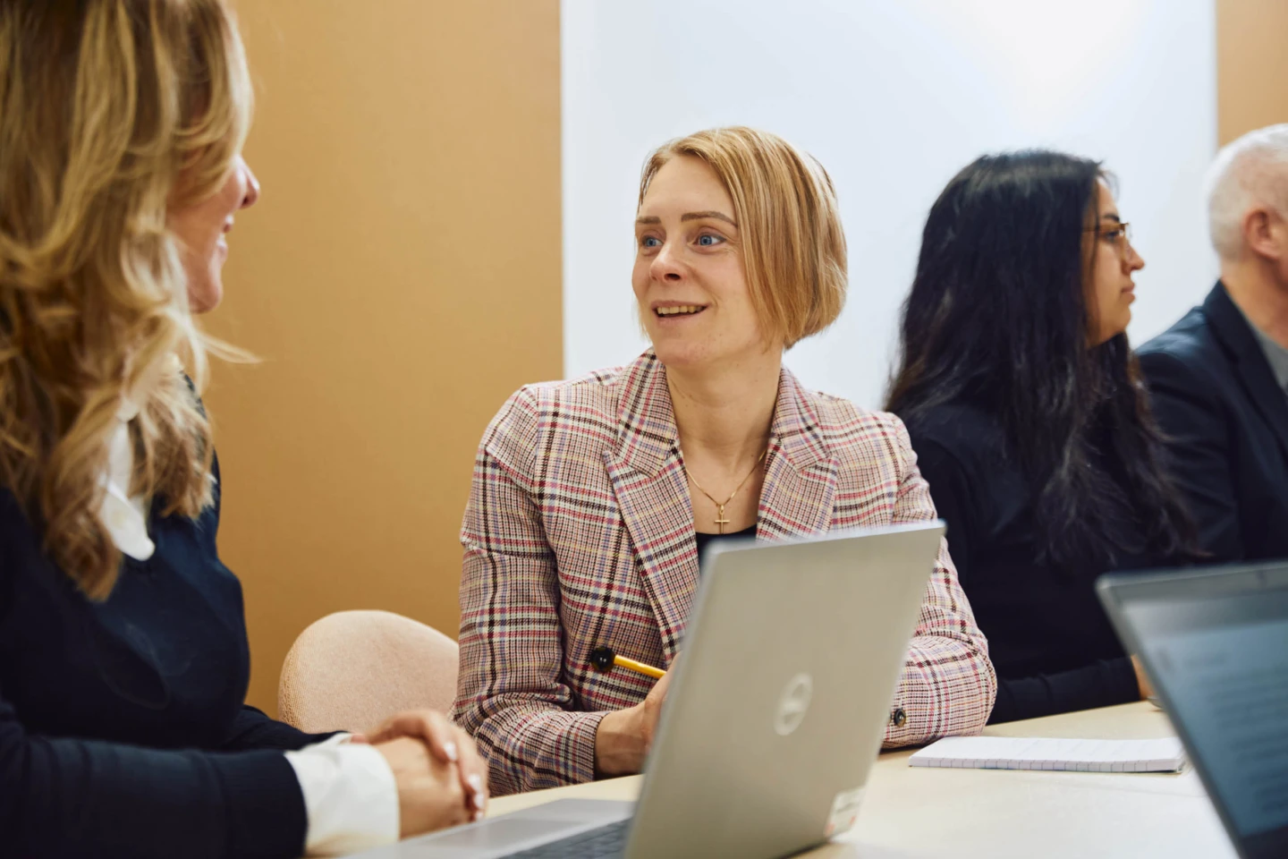Två kollegor samtalar vid ett möte med datorer framför sig.