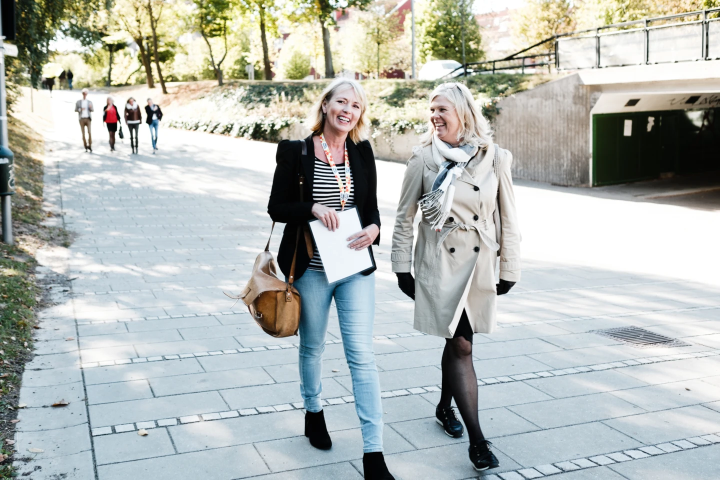 Två kvinnor promenerar och pratar glädjefyllt längs en gångväg.