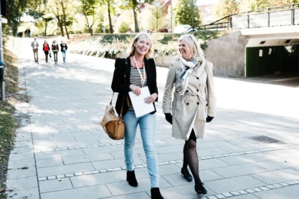 Två kvinnor promenerar och pratar glädjefyllt längs en gångväg.